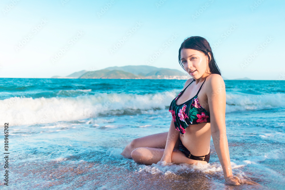 Beautiful pretty sexy hot girl posing, lying on the sand, swimming in the sea, water. Young brunette woman in bikini, swimsuit relaxing on beach. Lady on vacation in tropic island. Summer, blue sky.