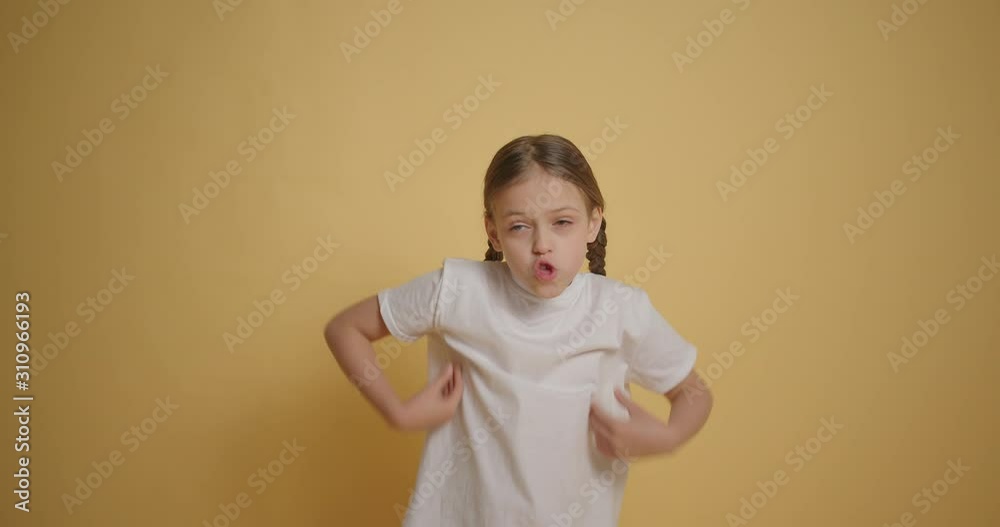 Little girl in white t-shirt making funny face at yellow background slow motion
