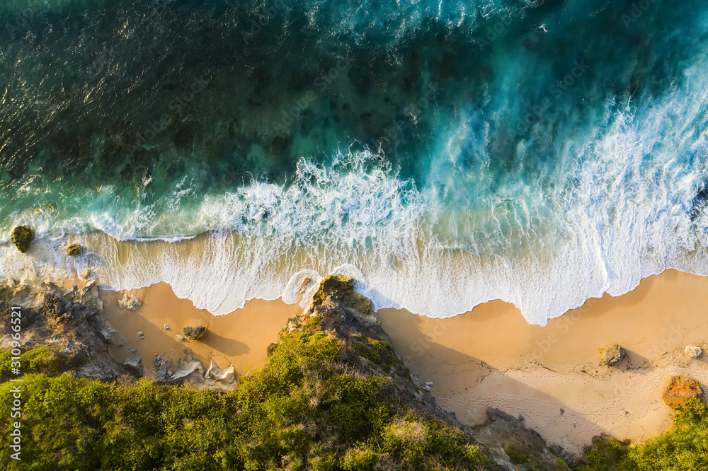 View from above, stunning aerial view of a rocky shore with a beautiful beach bathed by a rough sea during sunset, Nyang Nyang Beach (Pantai Nyang Nyang), South Bali, Indonesia.