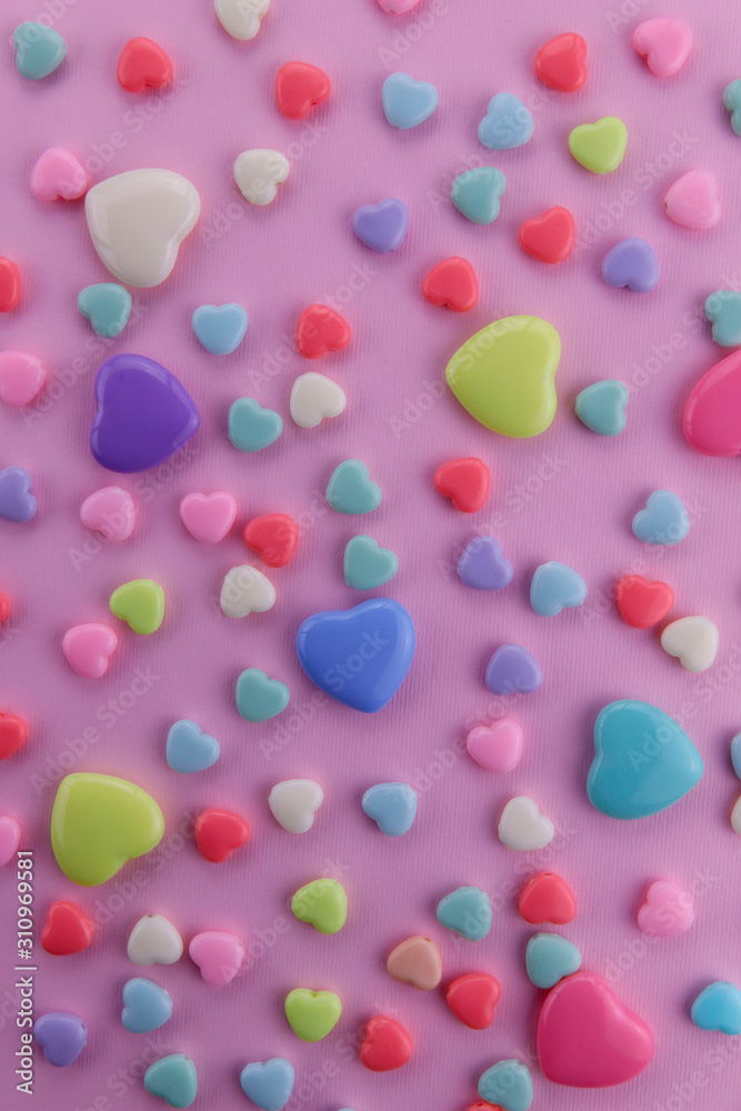 On a pink background there are many small and large hearts of different colors. Yellow, red, blue and green hearts on a pink background. Vertical, close-up. Valentine's day. On a pink background there are many small and large hearts of different colors. Yellow, red, blue and green hearts on a pink background. Vertical, close-up. Valentine's day.