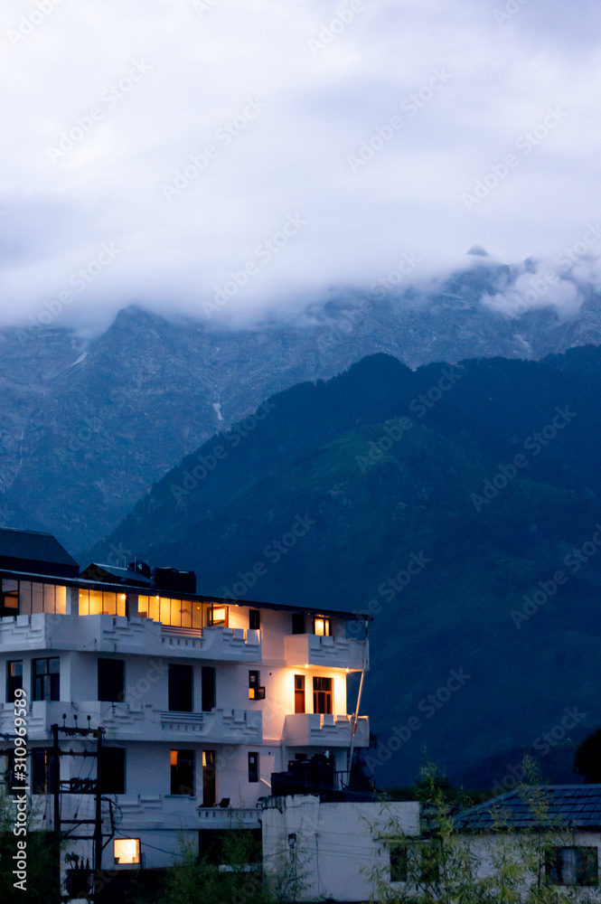 The warm lights from a building against the cool backdrop of fog covered mountains in the hill station of McLeodganj India