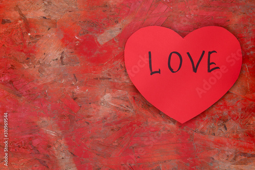 FLAT LAY STYLE. On a red old wooden surface, a red heart with the inscription LOVE. A lot of free space, horizontal, close-up. Valentine's Day.