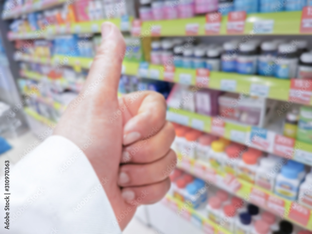 Blurry picture of hand with thumbs up with shelves full of supplements and medicine in the background