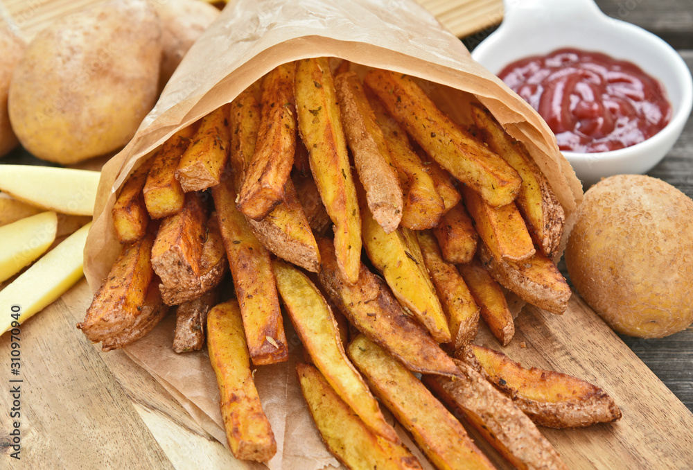 Homemade Crispy Seasoned French Fries..French fries  with spicy seasoning in brown paper bag on wooden broad.