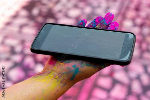 young girl with colored gulaal powder on her hands holding a mobile phone during the festival of holi photo