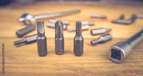 Set of bits for screwdriver. Metal bits for screwdriver. Tool set for household use. Nozzles and adapters for screwdrivers. Different size hex driver. Wooden background. Repair concept.
