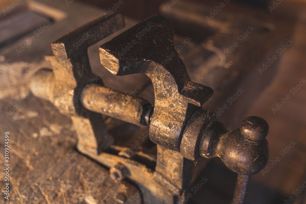 An old used vintage metal vise on a wood workbench. Close up photo.