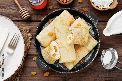 Thin pancakes or crepes stuffed with cottage cheese and raisins on wooden background. top view photo