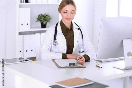 Young woman doctor at work in hospital looking at desktop pc monitor. Physician controls medication history records and exam results. Medicine and healthcare concept