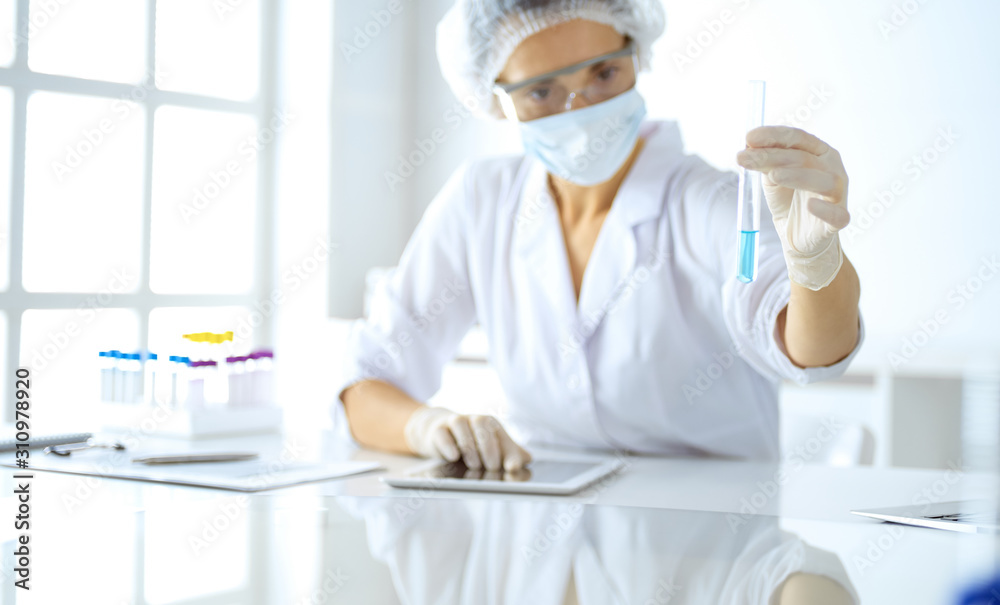Professional female scientist in protective eyeglasses researching tube with reagents in laboratory. Concepts of medicine and research Professional female scientist in protective eyeglasses researching tube with reagents in laboratory. Concepts of medicine and research