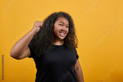 Strict afro-american young lady with overweight over isolated orange background wearing fashion black shirt showing fist at camera, fight. People lifestyle concept.