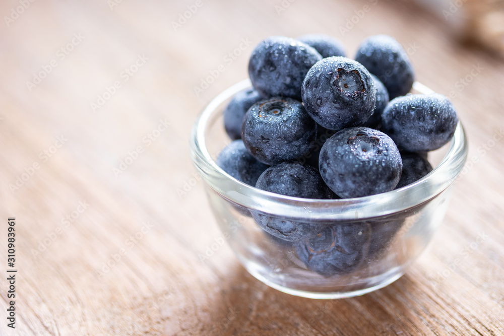 Blueberries in a glass bowl on wooden table and texture, fresh fruit with water droplet