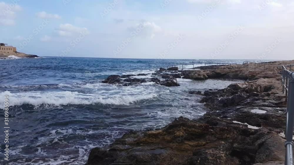 Foamy sea waves washing on the rocky coast of the mediterranean sea. Maltese seashore with handrails background with copy space Foamy sea waves washing on the rocky coast of the mediterranean sea. Maltese seashore with handrails background with copy space