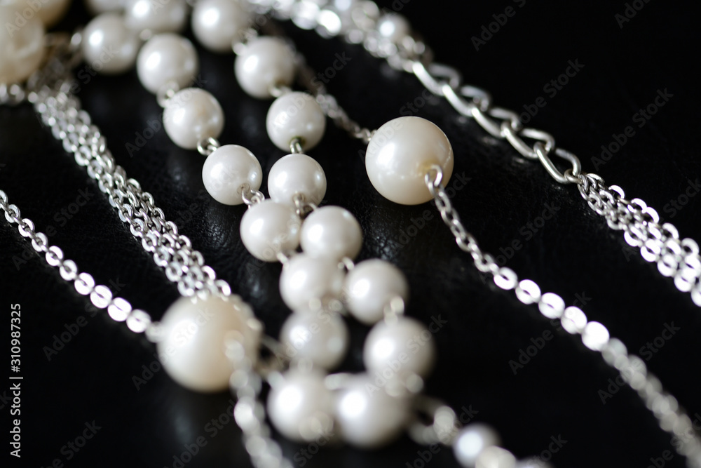 Modern necklace made of silver chains and white beads close-up on a dark surface. Fashion background Modern necklace made of silver chains and white beads close-up on a dark surface. Fashion background