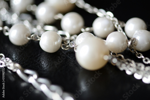 Modern necklace made of silver chains and white beads close-up on a dark surface. Fashion background