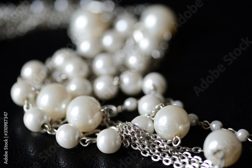Modern necklace made of silver chains and white beads close-up on a dark surface. Fashion background