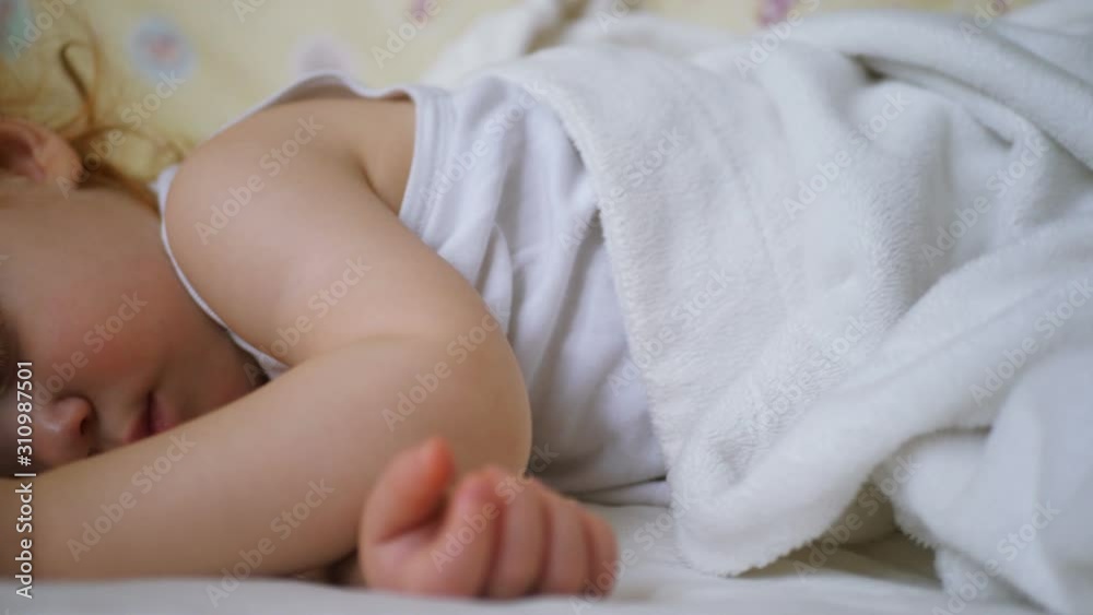 Cute infant baby under blanket on bed with white linen sleeping dreamily Cute infant baby under blanket on bed with white linen sleeping dreamily