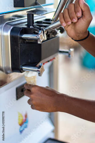 Human hand holding cone with twisted ice cream from machine