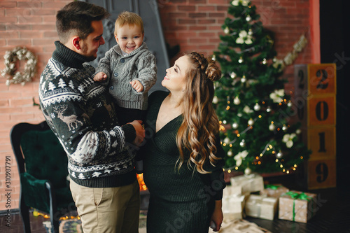 Beautiful family sitting near Christmas tree. Cute mother in a green dress. Little boy with handsome father