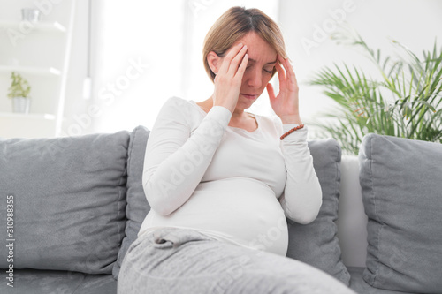 Pregnant tired exhausted woman with stomach and head issues at home on a couch, being sick.