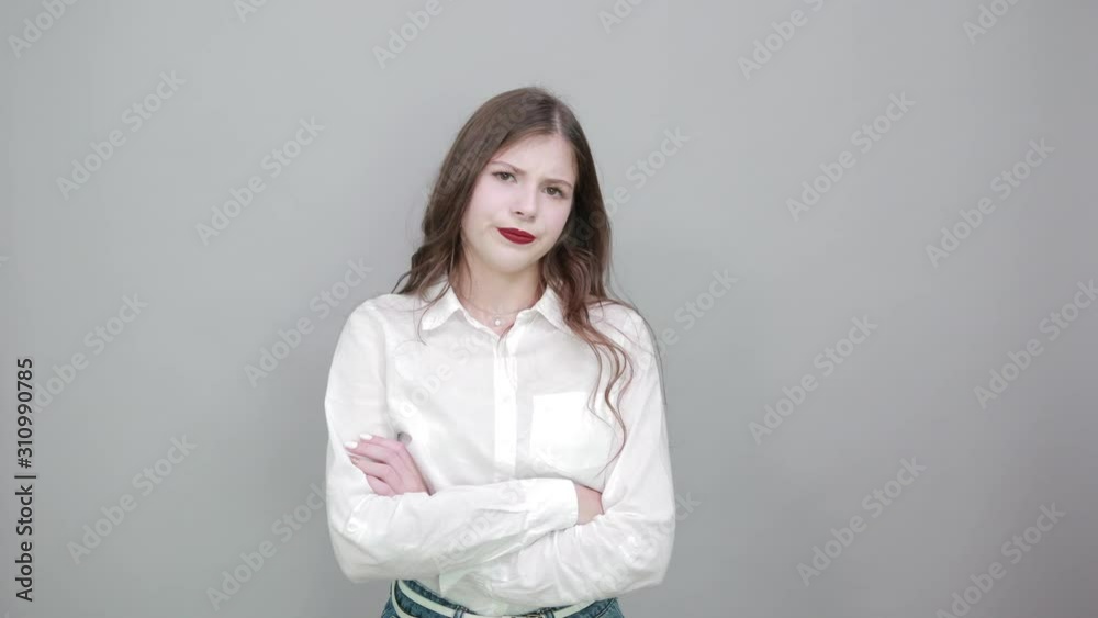 Caucasian young brunette woman over isolated gray background wearing casual white shirt, looking disappointed, keeping hands crossed, looking at camera. People lifestyle concepte. Caucasian young brunette woman over isolated gray background wearing casual white shirt, looking disappointed, keeping hands crossed, looking at camera. People lifestyle concepte.