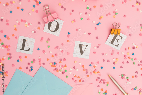 Valentines day concept with Love word made of paper cards, envelope and colorful confetti on pink background. Flat lay