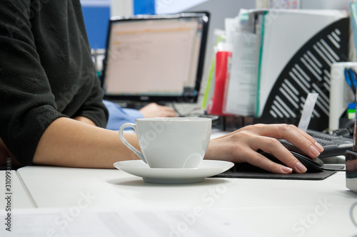 White tea cup with hand on computer desk in office