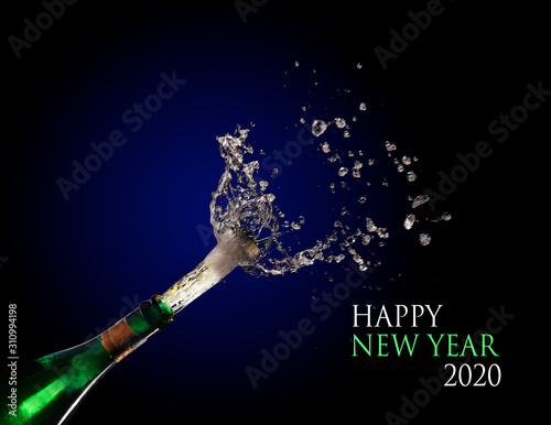 Happy New Year 2020 text and a champagne bottle exploding and shooting out the cork with splashes against a dark blue background, copy space