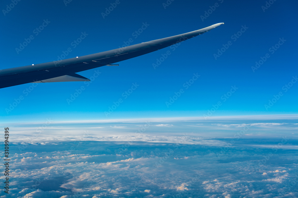 Fototapeta premium At sunrise wing of an airplane flying above the clouds