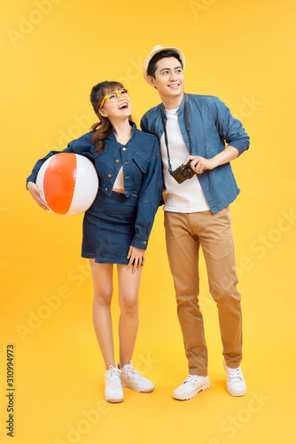 Lovely Asian couple in summer casual clothes with beach accessories isolated on colorful yellow banner background with copy space © makistock