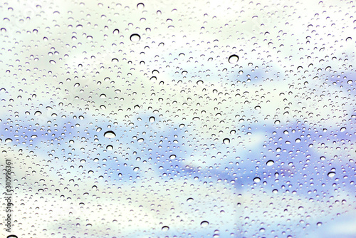 Closeup and crop rain drop on glass and blurry light blue background