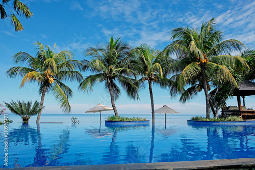 Luxury infinity swimming pool with blue water  umbrellas  palms and endless ocean view. Bali  Indonesia.