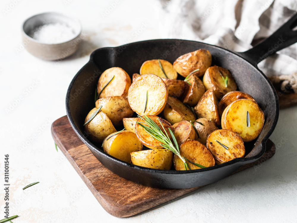 Black cast iron pan with fried roasted potato wedges with herbs on a light background Black cast iron pan with fried roasted potato wedges with herbs on a light background