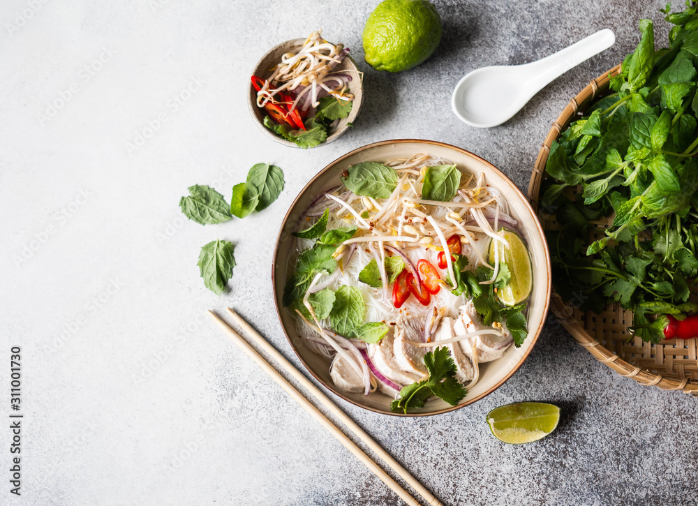 Traditional Vietnamese soup- pho ga in bowl with chicken and rice noodles, mint and cilantro, red onion, chili, bean sprouts and lime on grey background. Asian food. Copy space. Top view - obrazy, fototapety, plakaty 