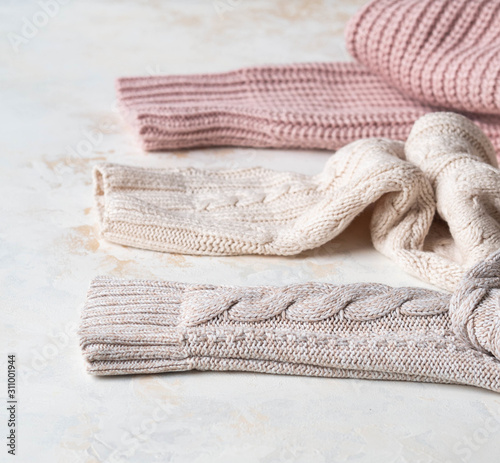 Sleeves of three of warm different knitted woolen sweaters pastel shades beige textured background.