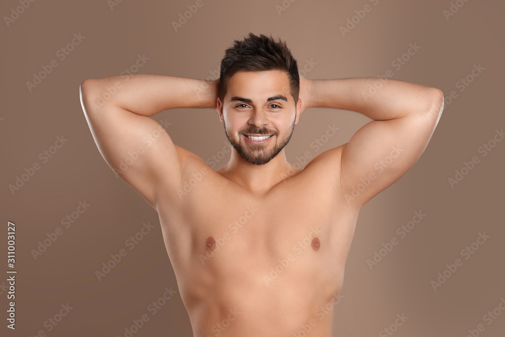 Young man showing hairless armpits after epilation procedure on brown background