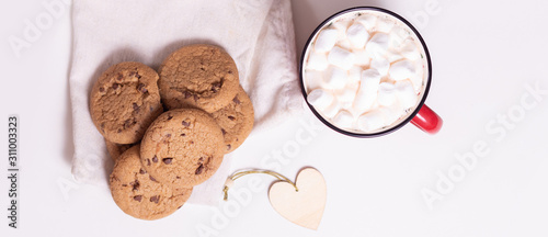 Red mug with cocoa and marshmallows and homemade cookies with chocolate, wooden heart - Christmas tree toy on a light background
