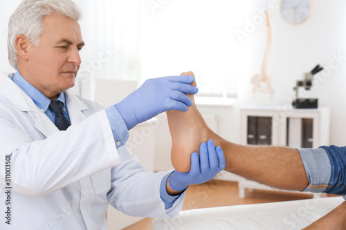 Male orthopedist checking patient's foot in clinic photo