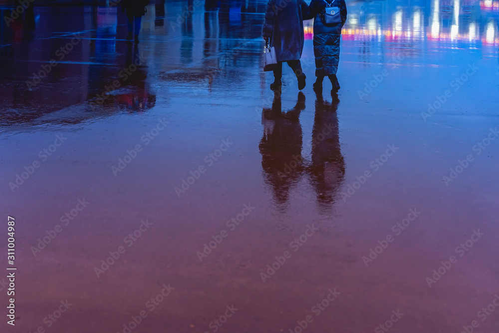Silhouettes of abstract young and elderly woman hurrying in the rain back to us, their reflection in the wet asphalt, in a puddle, concept of seasons, weather, lifestyle
