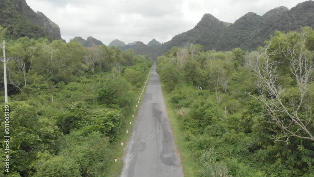 Aerial: people riding scooter inland Cat Ba island, travel destination in Vietnam. People driving motorbike on road through lush green jungle and karst mountain range. native cinelike d-log flat color Aerial: people riding scooter inland Cat Ba island, travel destination in Vietnam. People driving motorbike on road through lush green jungle and karst mountain range. native cinelike d-log flat color