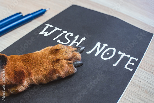 Ginger dog paw on wish note at the table. Wish list or new year resolution concept.