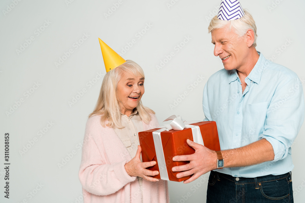 cheerful senior husband and wife holding red gift box isolated on grey cheerful senior husband and wife holding red gift box isolated on grey