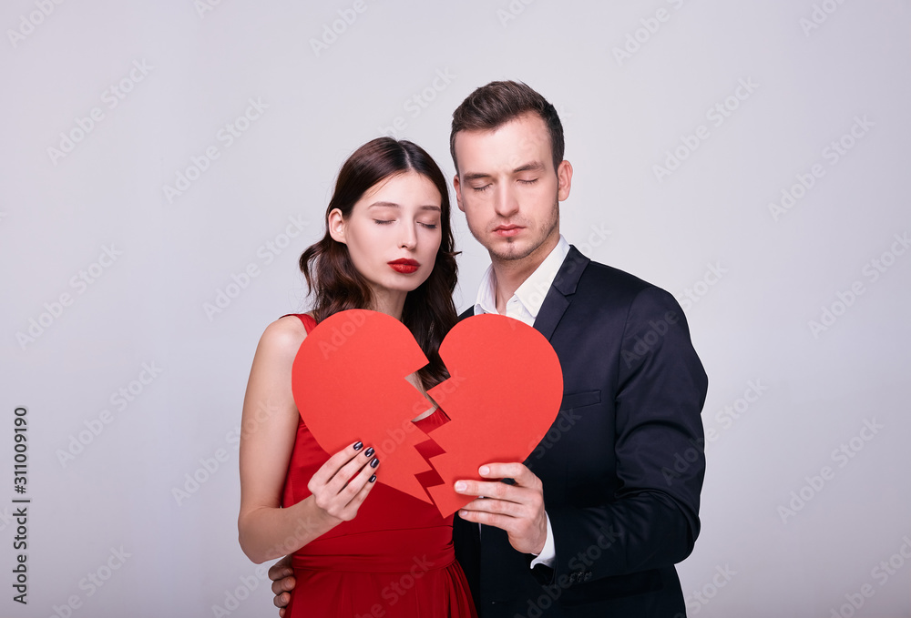 Elegant couple in stylish clothes with a broken red heart on a white background.