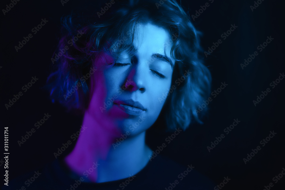 portrait of a girl with eyes closed with curls on a black studio background. in the light of colored lamps. Happy girl portrait of a girl with eyes closed with curls on a black studio background. in the light of colored lamps. Happy girl