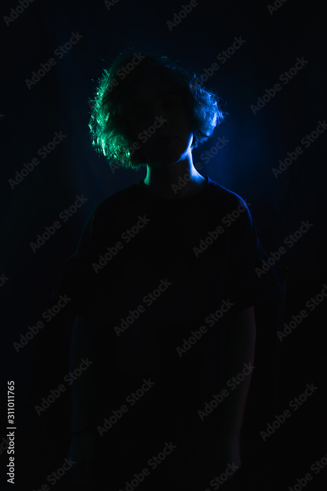 blue-green silhouette of a girl with curls on a black studio background. in the light of colored lamps. blue-green silhouette of a girl with curls on a black studio background. in the light of colored lamps.