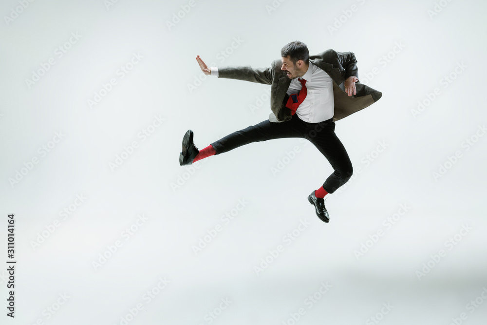 Young caucasian man moving flexible on white studio background. Male model in office attire bending over, avoiding something, catched in motion and action. Looks angry, scared, fighting. Emotions.