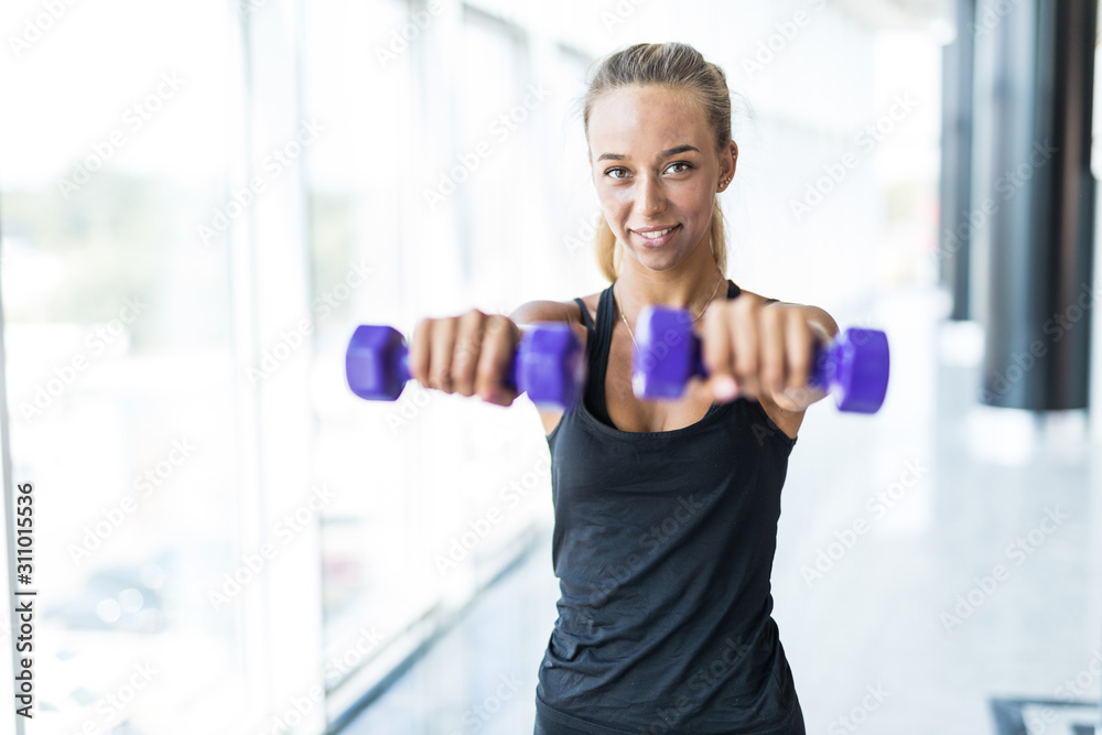 Fototapeta premium Slim young beautiful girl warming up with weights in health club.