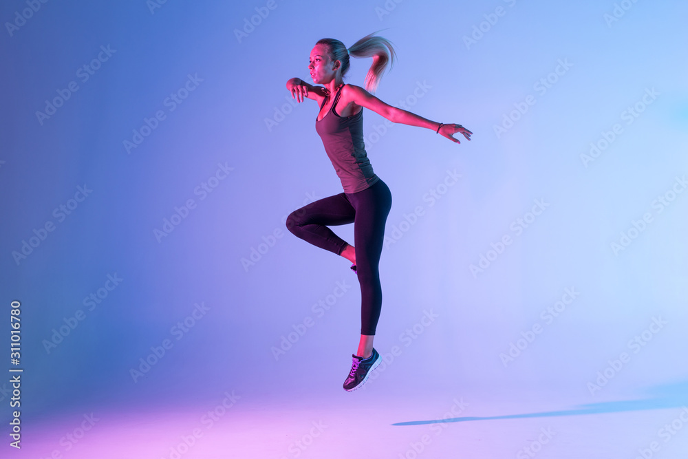 Handsome woman with perfect body jumping against colorful trendy background. Young athletic girl in jump