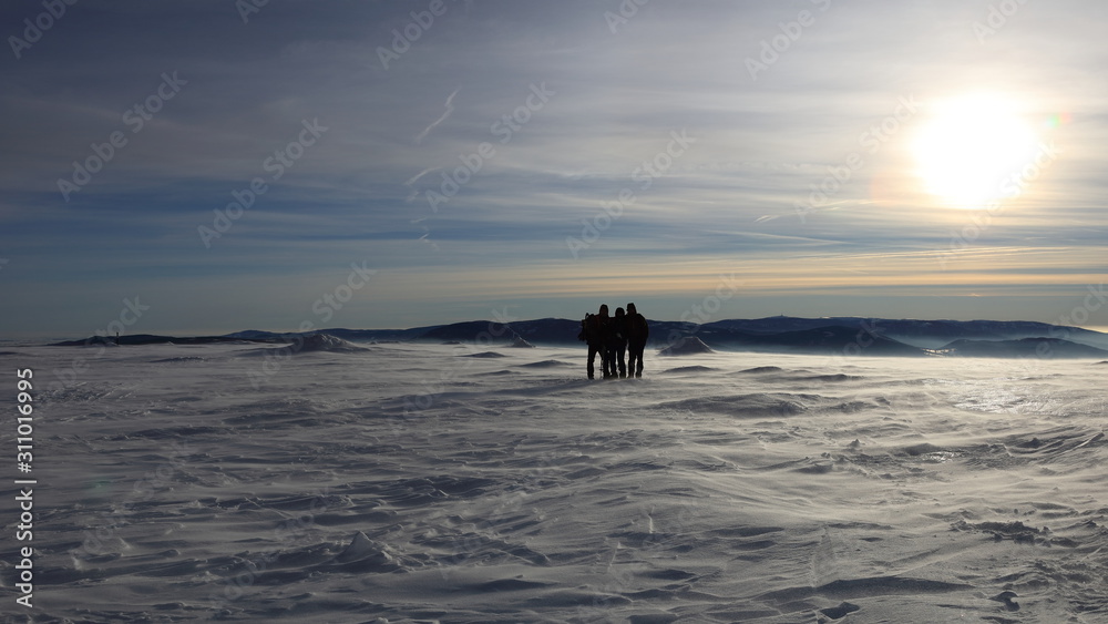 Silhouettes of three people at the top of snow covered mountain at the end of a day during sunset. Silhouettes of three people at the top of snow covered mountain at the end of a day during sunset.