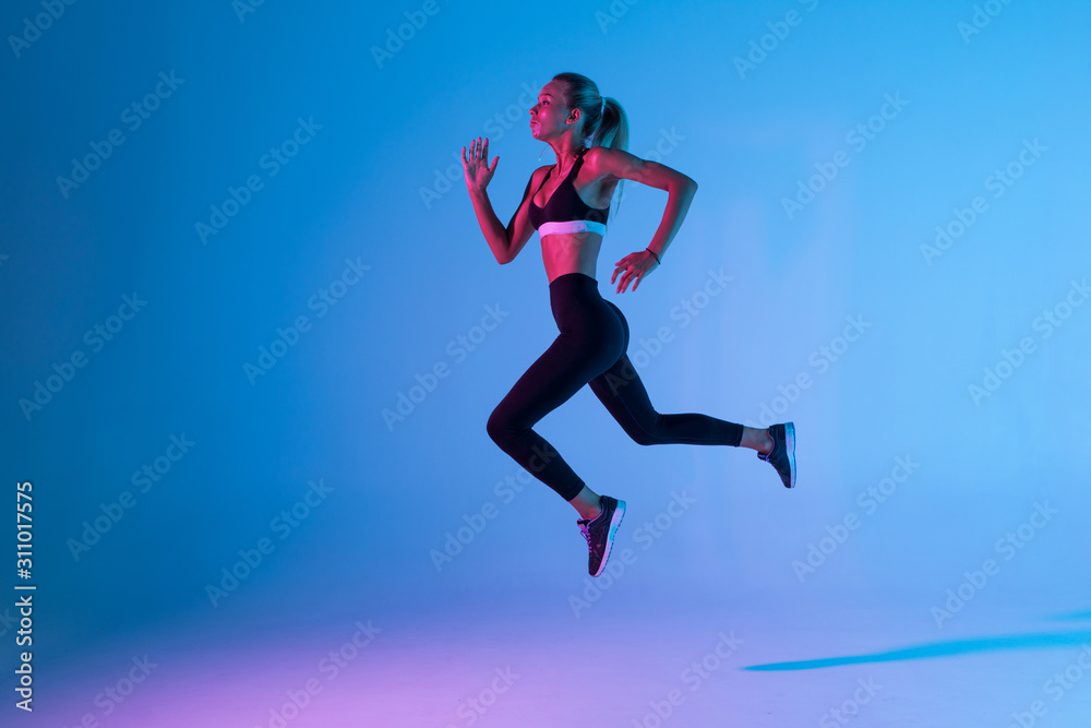 Sporty young woman fitness jumping isolated on purple light background